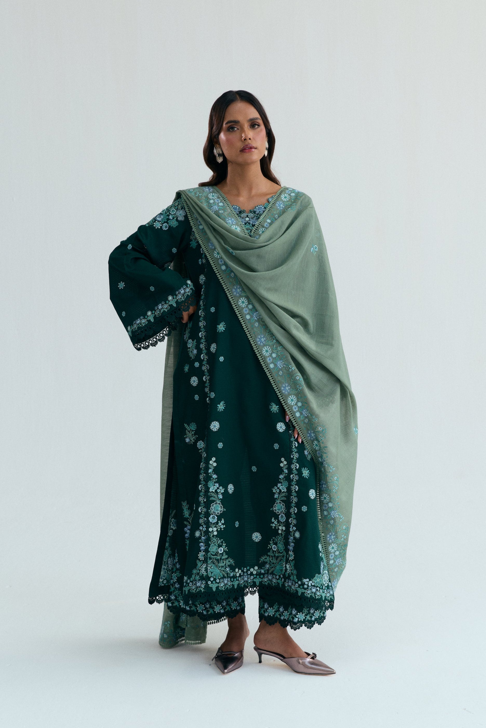 Deep green Pakistani three piece outfit with embroidered long shirt, lace-detailed izaar trousers, and contrasting pastel dupatta. Perfect for Eid.
