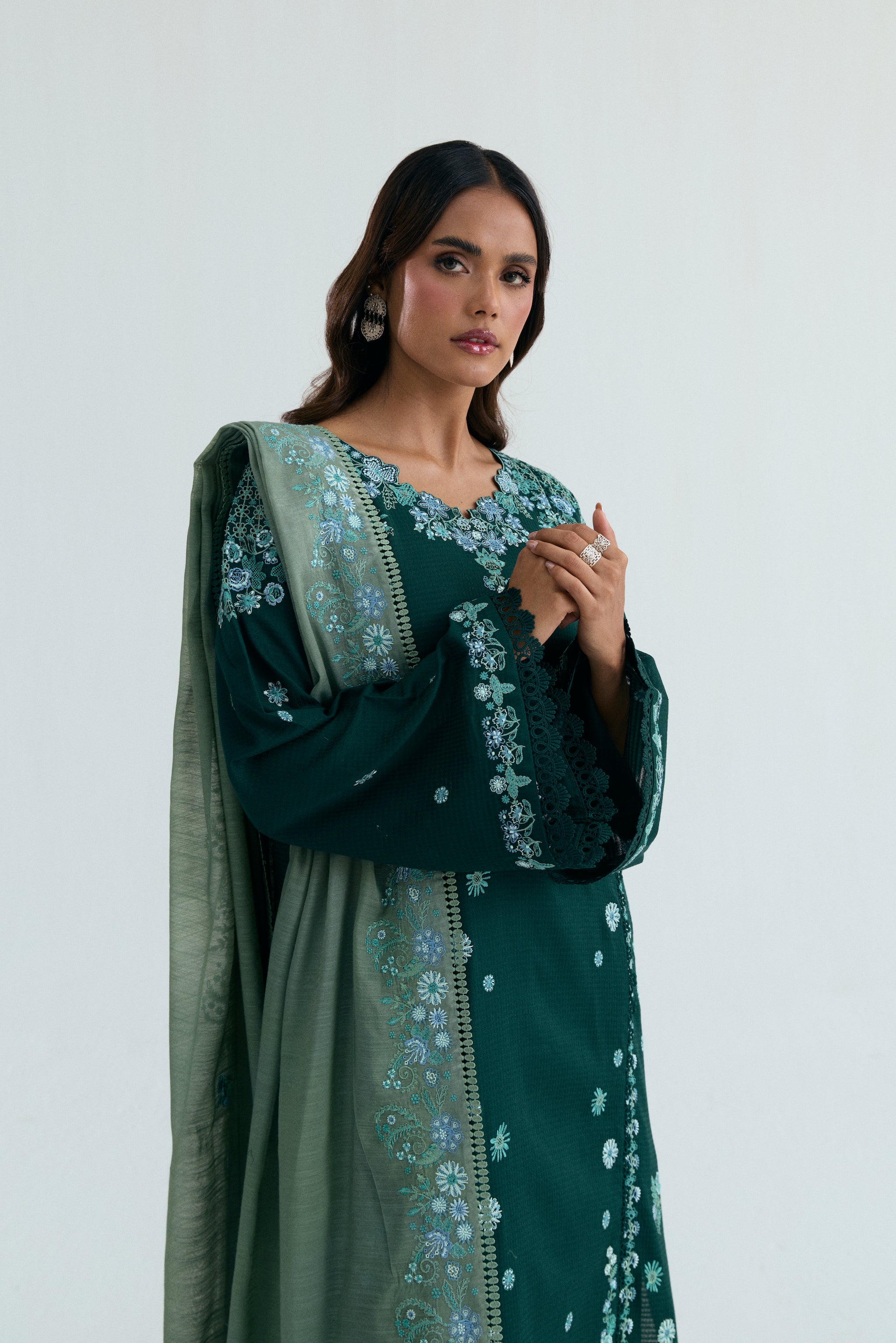 Deep green Pakistani three piece outfit with embroidered long shirt, lace-detailed izaar trousers, and contrasting pastel dupatta. Perfect for Eid.