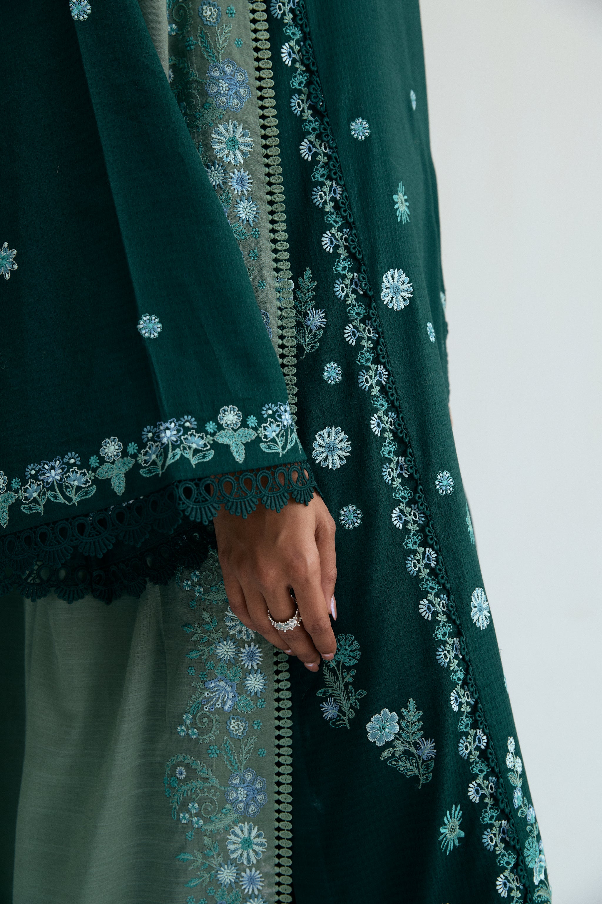 Deep green Pakistani three piece outfit with embroidered long shirt, lace-detailed izaar trousers, and contrasting pastel dupatta. Perfect for Eid.
