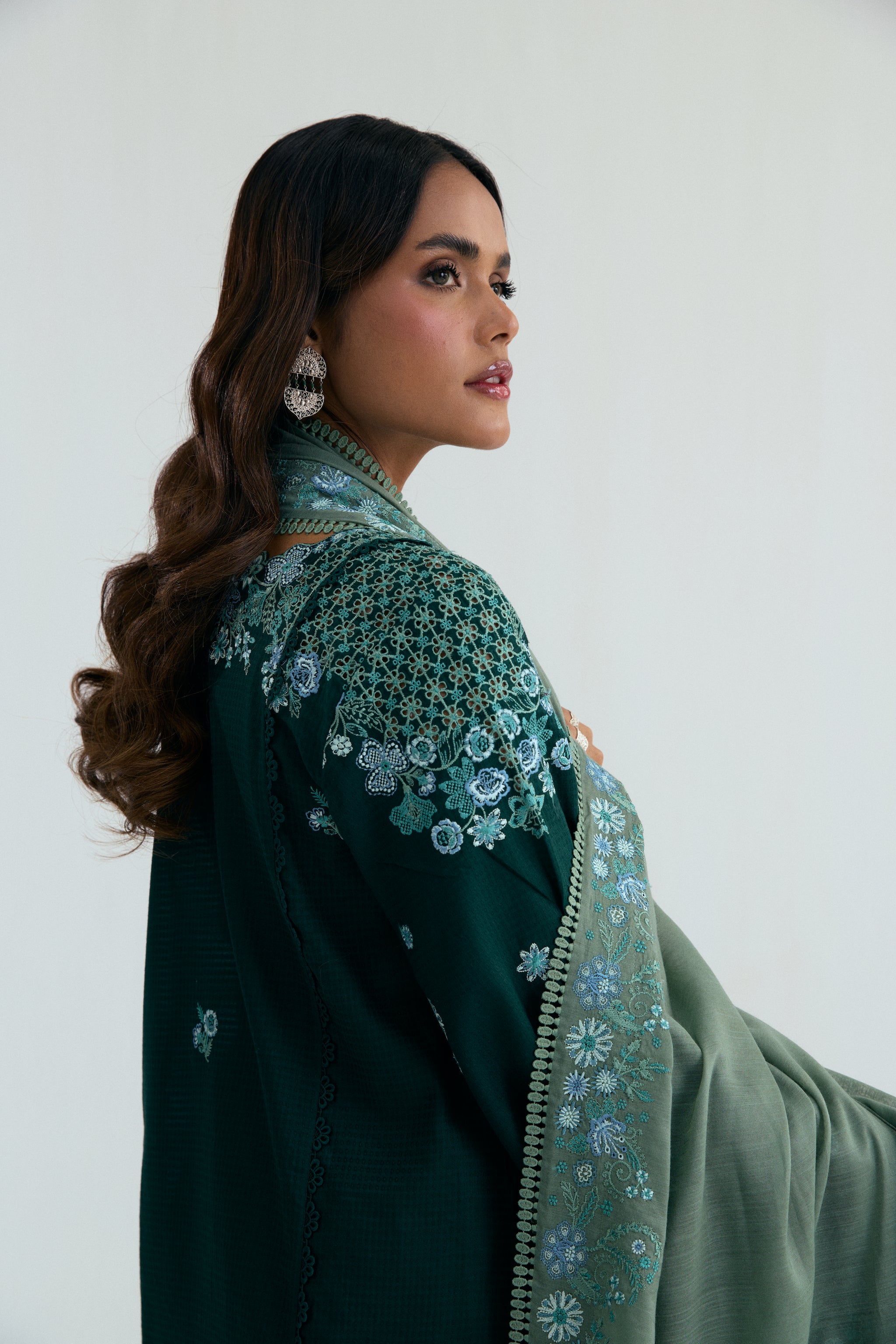 Deep green Pakistani three piece outfit with embroidered long shirt, lace-detailed izaar trousers, and contrasting pastel dupatta. Perfect for Eid.