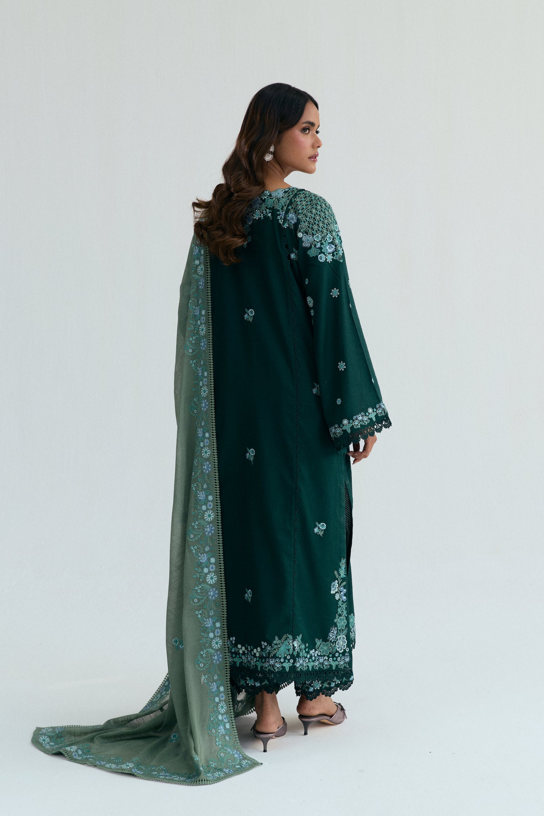Deep green Pakistani three piece outfit with embroidered long shirt, lace-detailed izaar trousers, and contrasting pastel dupatta. Perfect for Eid.