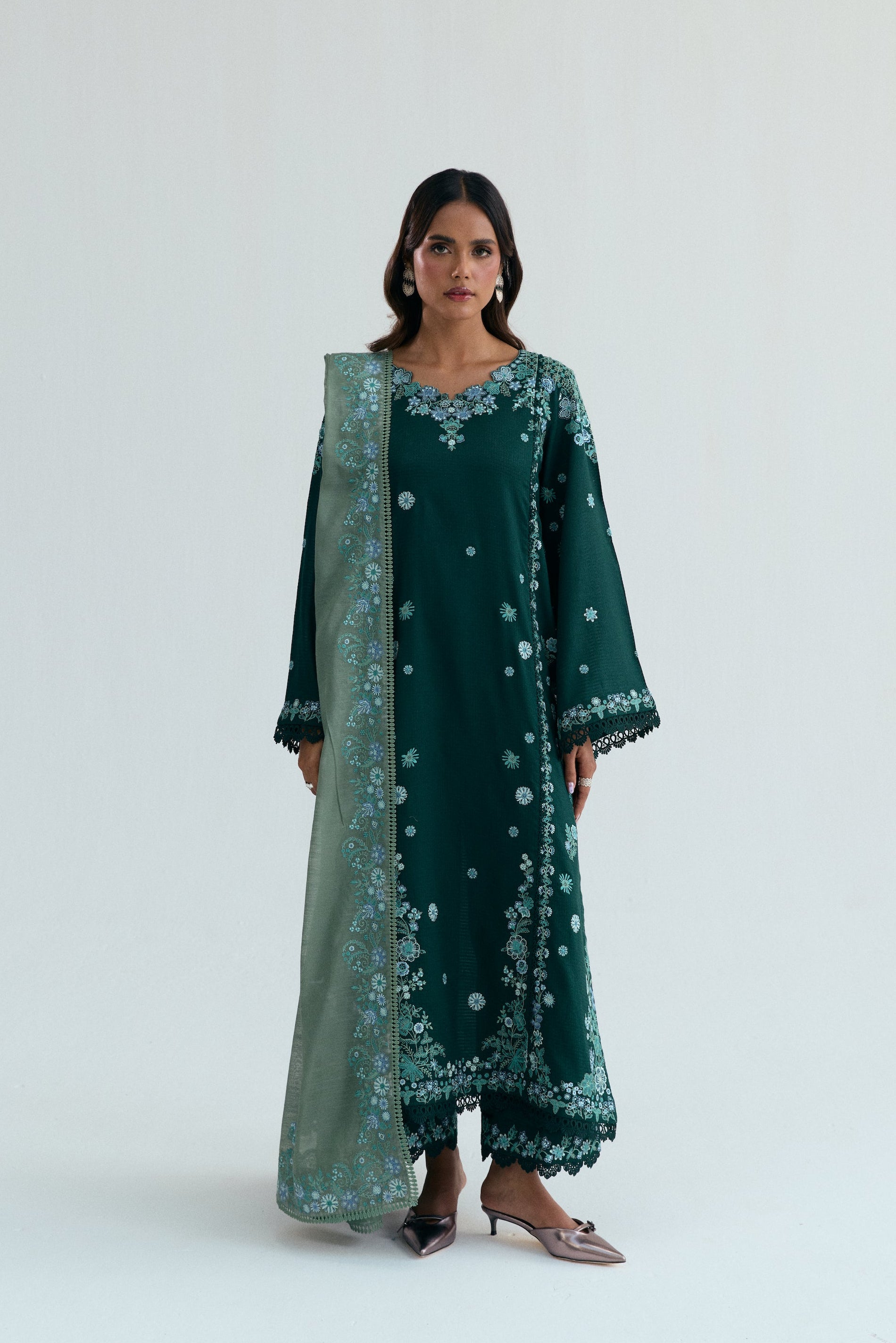 Deep green Pakistani three piece outfit with embroidered long shirt, lace-detailed izaar trousers, and contrasting pastel dupatta. Perfect for Eid.