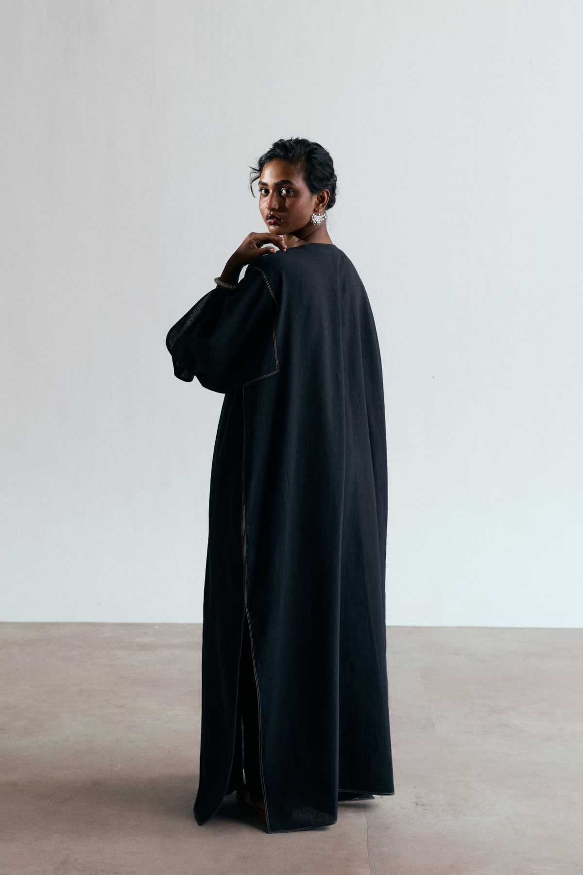 Back view of black kaftan with plain back panel, contrast seam stitching, wide sleeve and split side seam