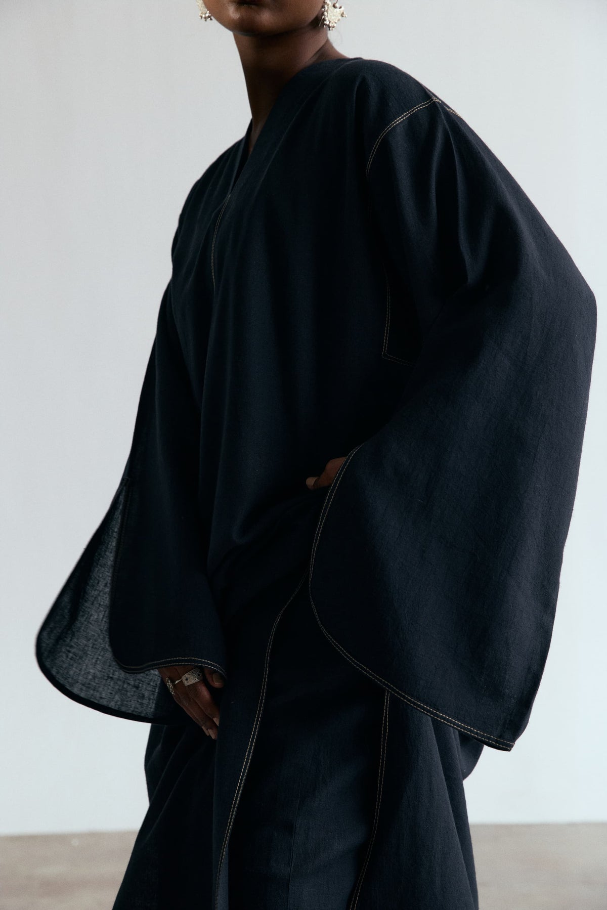 Wide slit sleeve with contrast accent stitching on a black linen-cotton kaftan, close-up detail