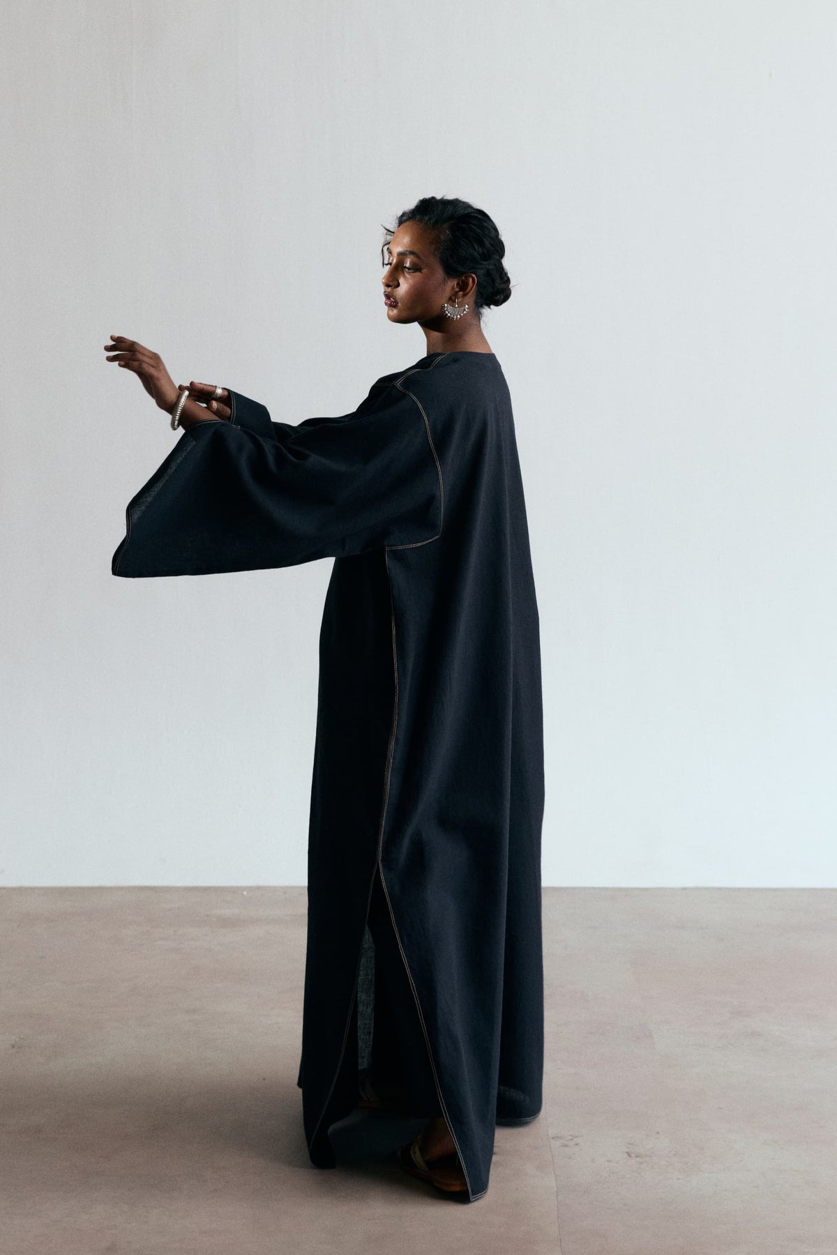 Side profile of black Pakistani kaftan with flared wide sleeve and accent stitching along the seams