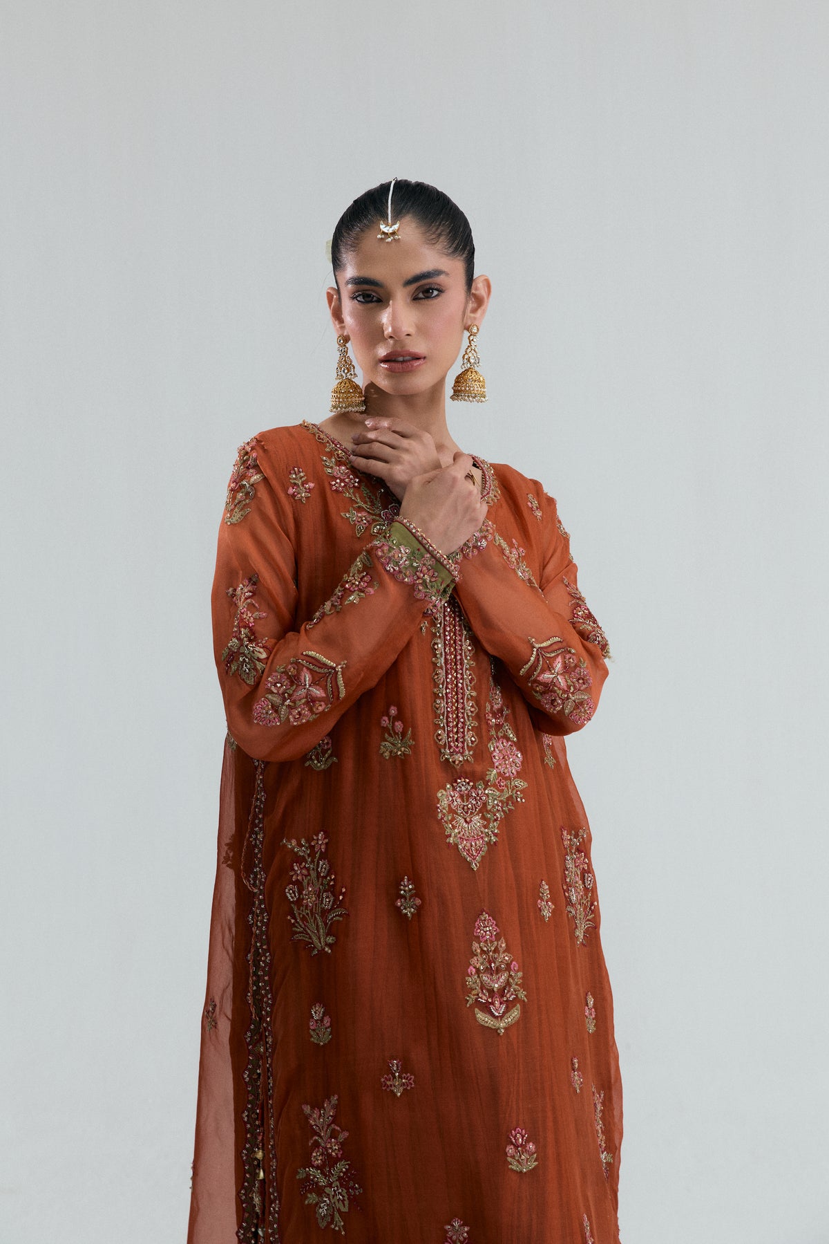 burnt orange Pakistani suit showing embellished sleeve cuffs, intricate V-neckline embroidery