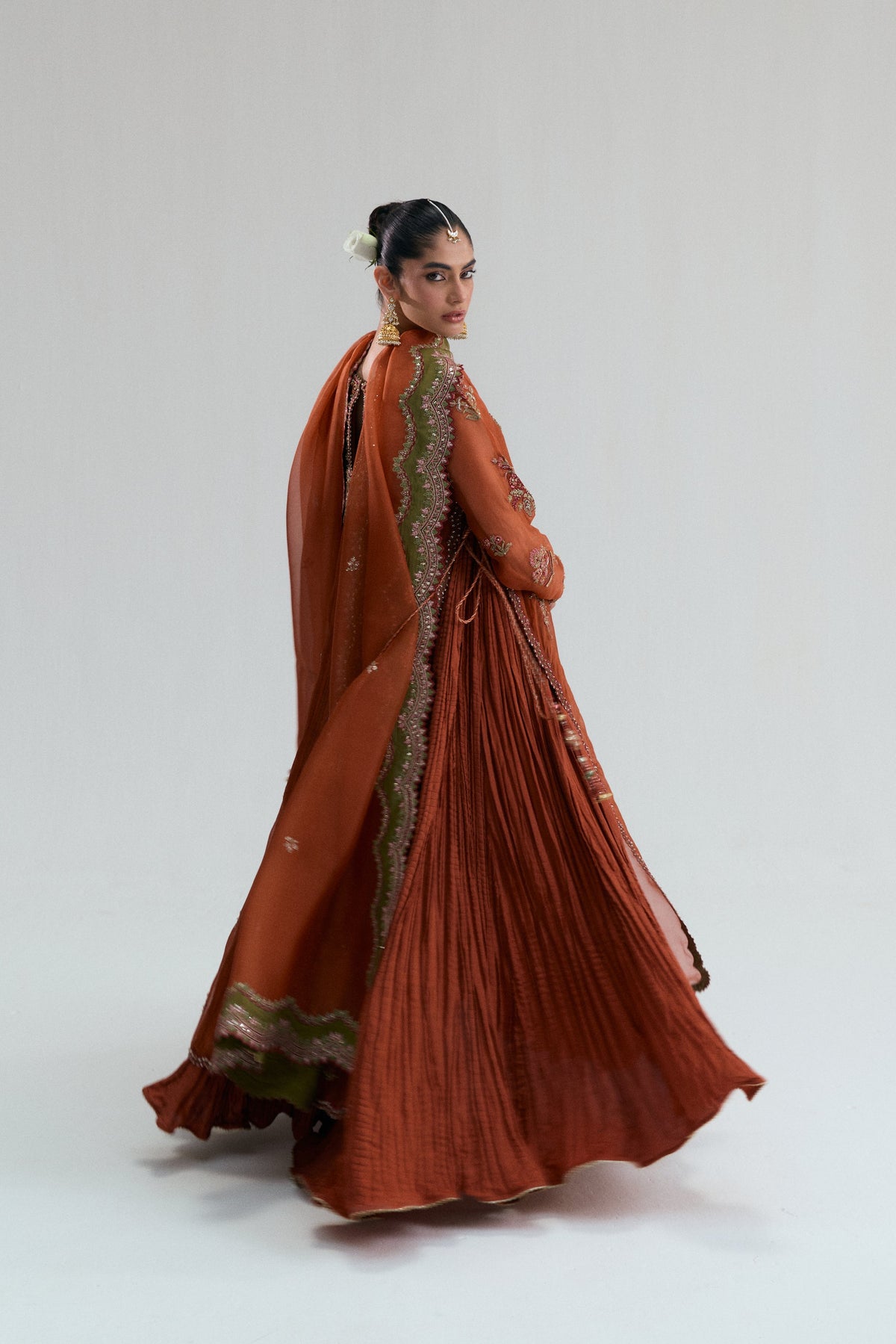 Burnt orange Pakistani outfit captured mid-turn, with the organza dupatta swirling behind