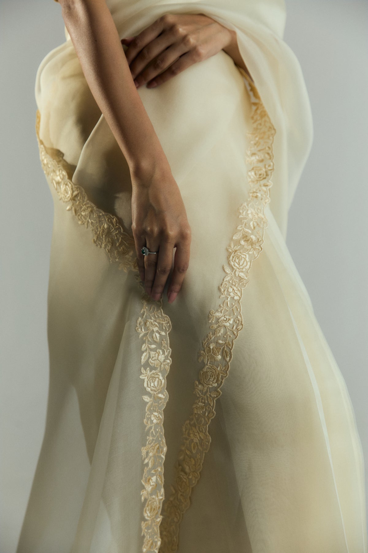 Detailed view of the gold floral embroidery on the pallu of an organza saree, held gently near the waist.