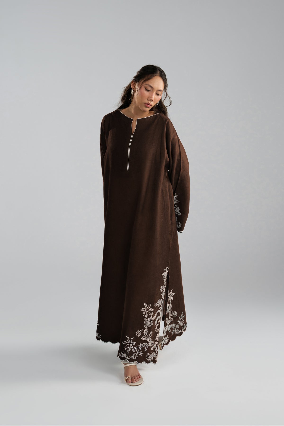 Long brown kaftan dress with a split neckline, front zipper and white floral embroidery near the hem.