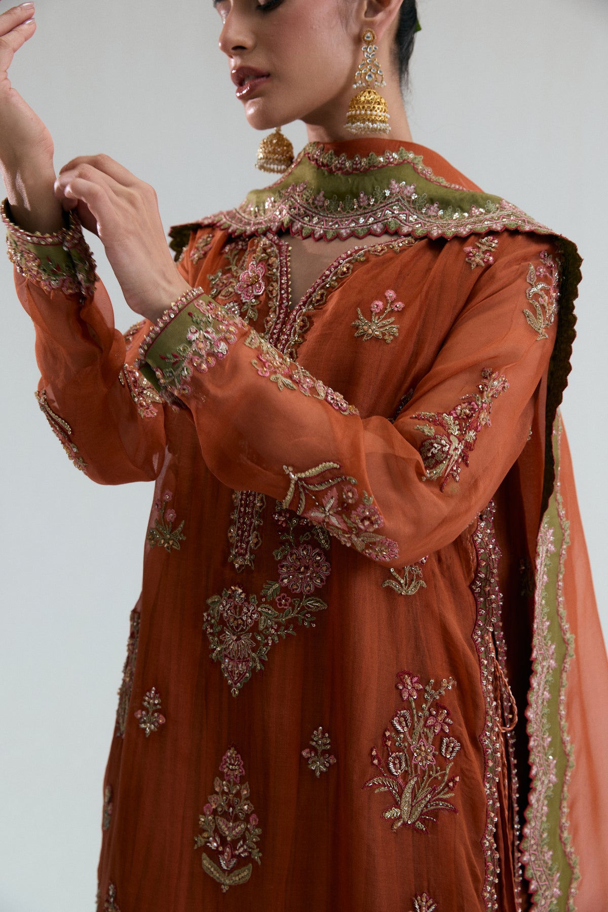 Side view of the embroidered shoulder, scalloped V-neckline, and dupatta detailing on the rust organza kameez