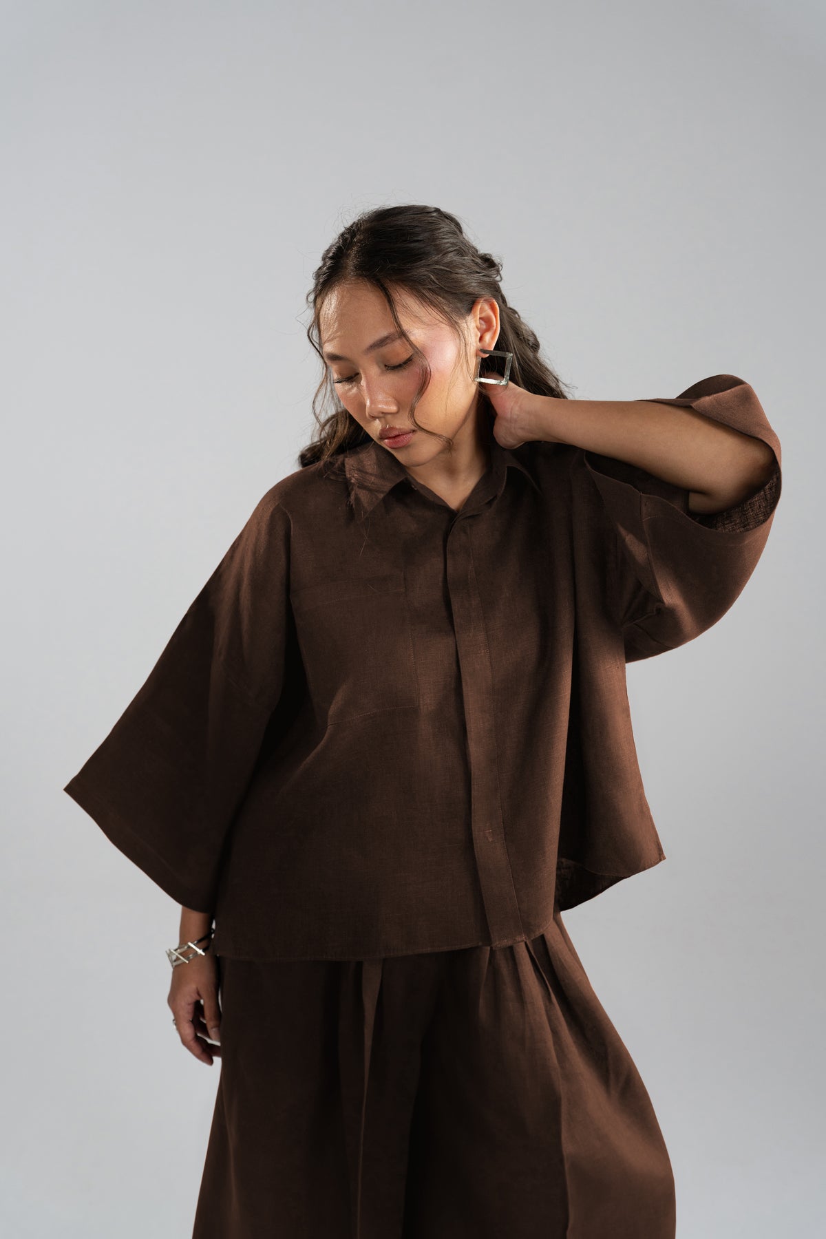 Editorial shot of a model wearing a loose brown oversized button-down top with wide kimono-style sleeves and matching trousers.