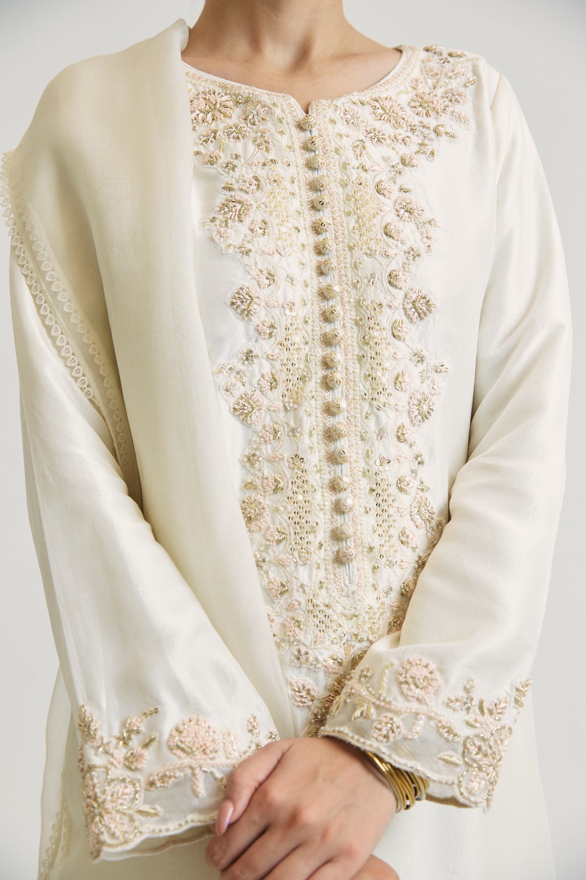 Close-up of the hand-embellished neckline on the ivory kameez, featuring hand-crafted embellishments; dense floral embroidery using pearls, gold thread and sequins adorns the area alongside the button placket.