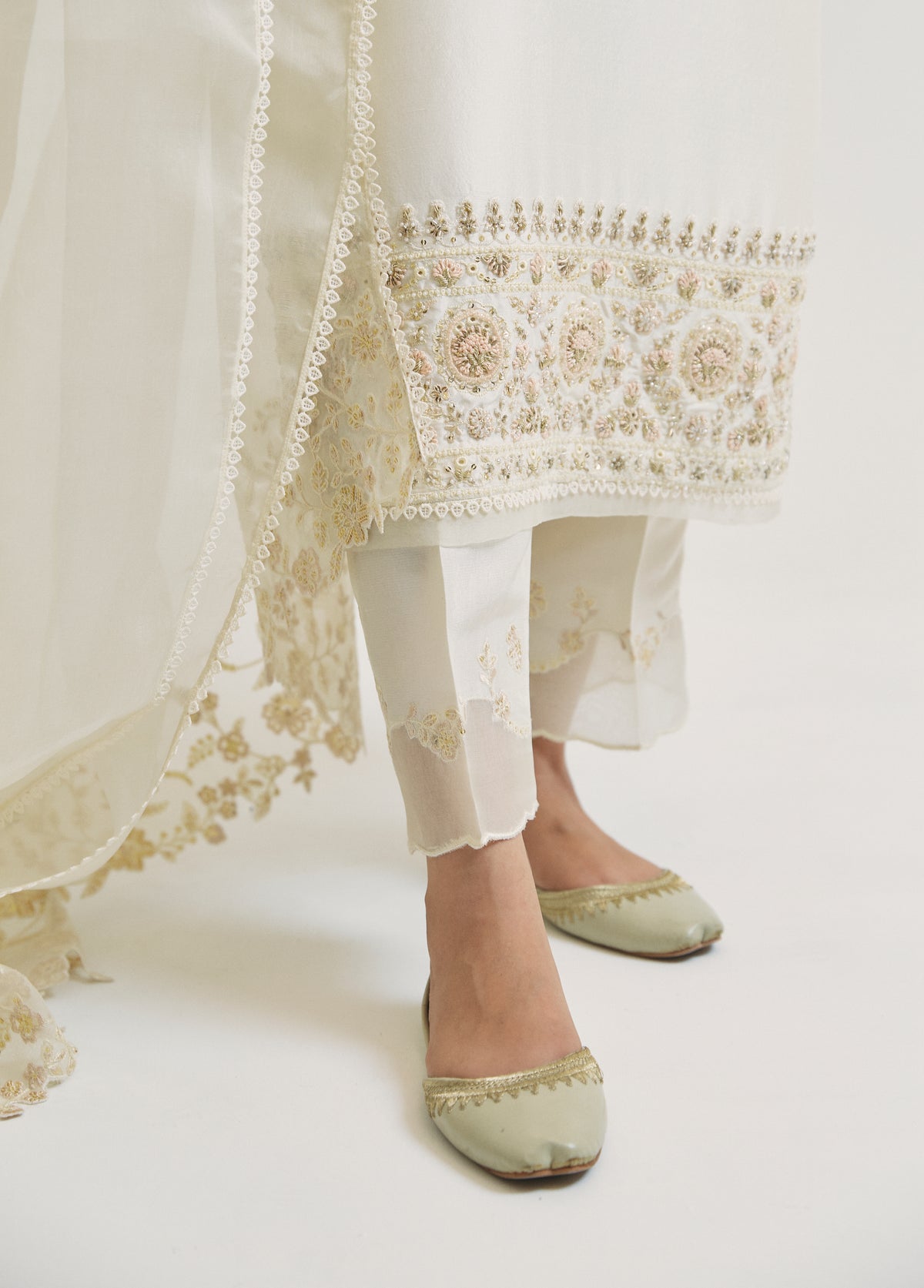 Close-up of the embroidered organza hem on the ivory raw silk trousers, featuring circular floral medallion embroidery, beadwork and lace trim.