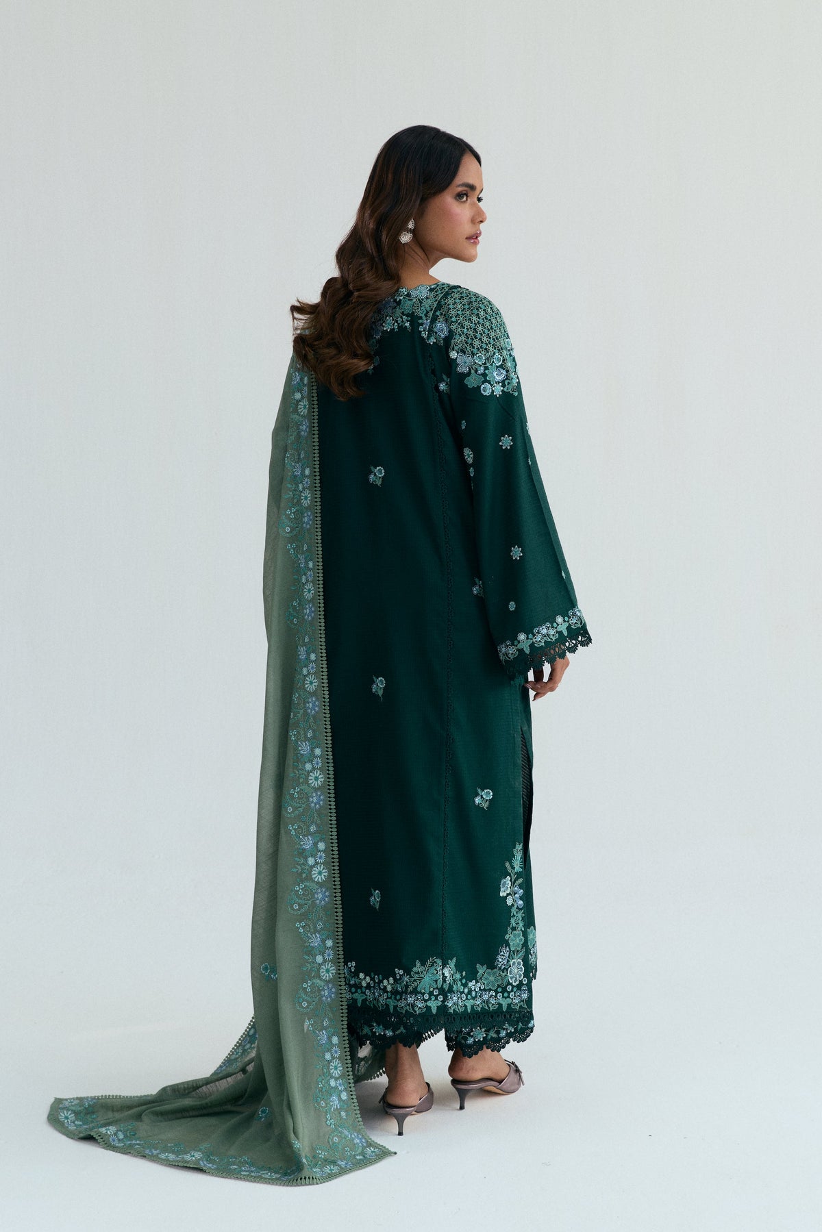 Back view of the deep green kameez featuring an embroidered border at the hem, with a light  green colored dupatta trailing behind.