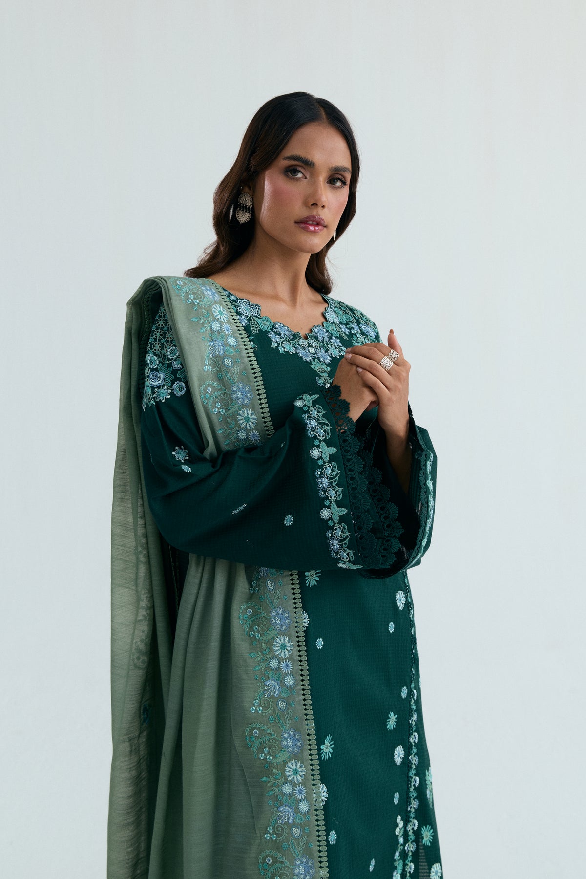 Close-up of the V-neckline featuring cutwork edges and floral embroidery, along with interlocked hands adorned with prominent rings.