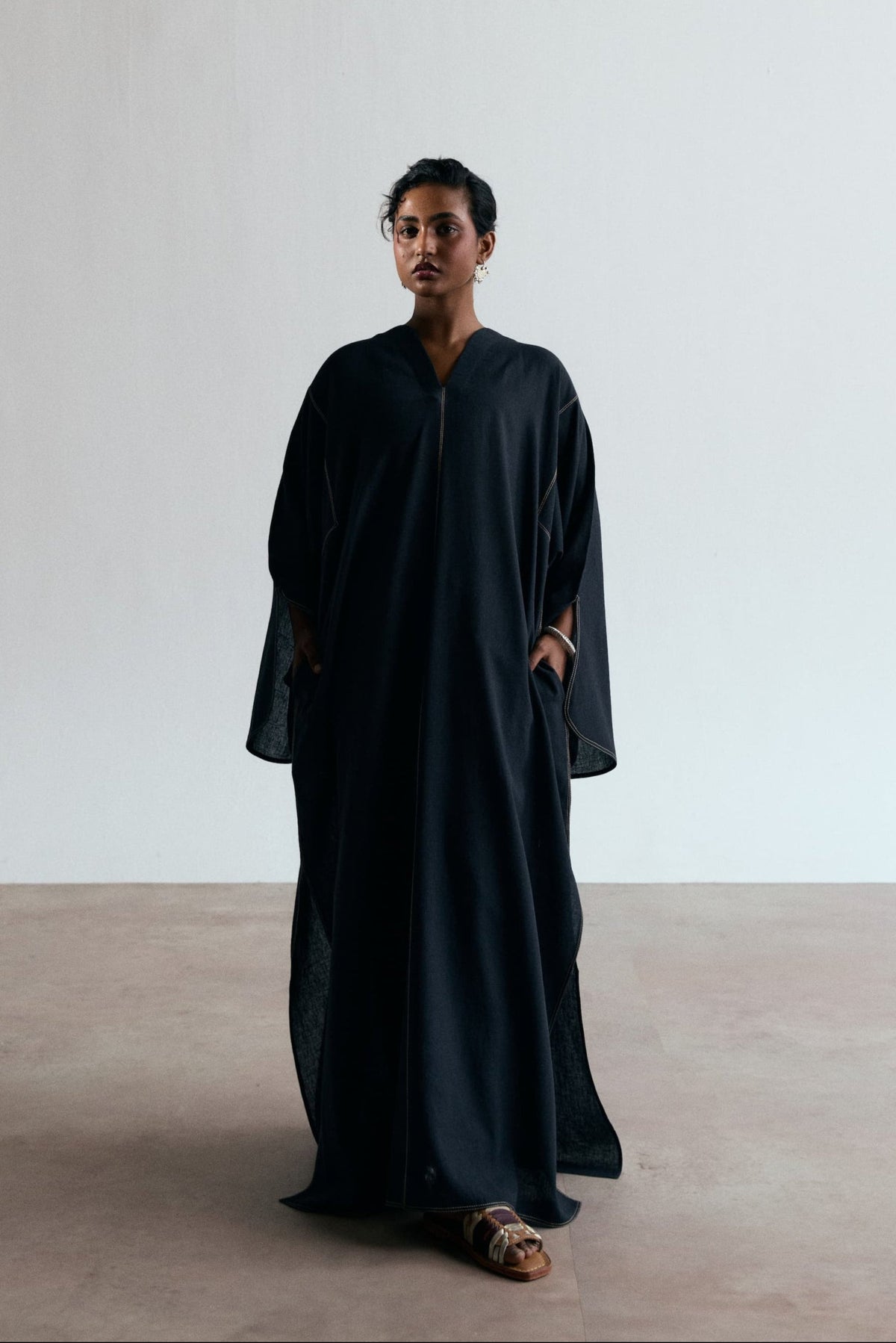 Long black kaftan with V-neckline, wide slit sleeves, contrast stitching and split side seams, full-length front view