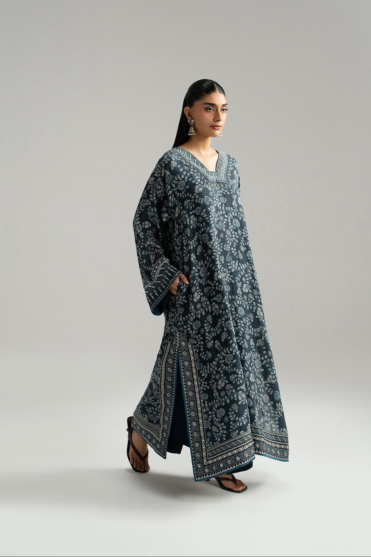 Walking view of navy blue phiran with wide sleeves, floral print and printed side slit border