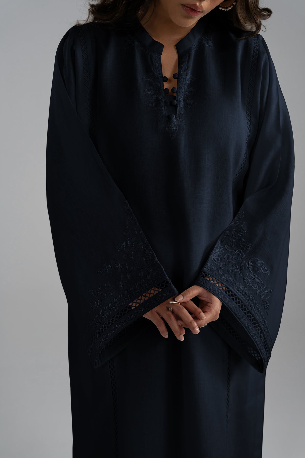 A close-up of a dark navy blue pure linen long-sleeved tunic dress with intricate embroidery and lace detailing on the cuffs and neckline.