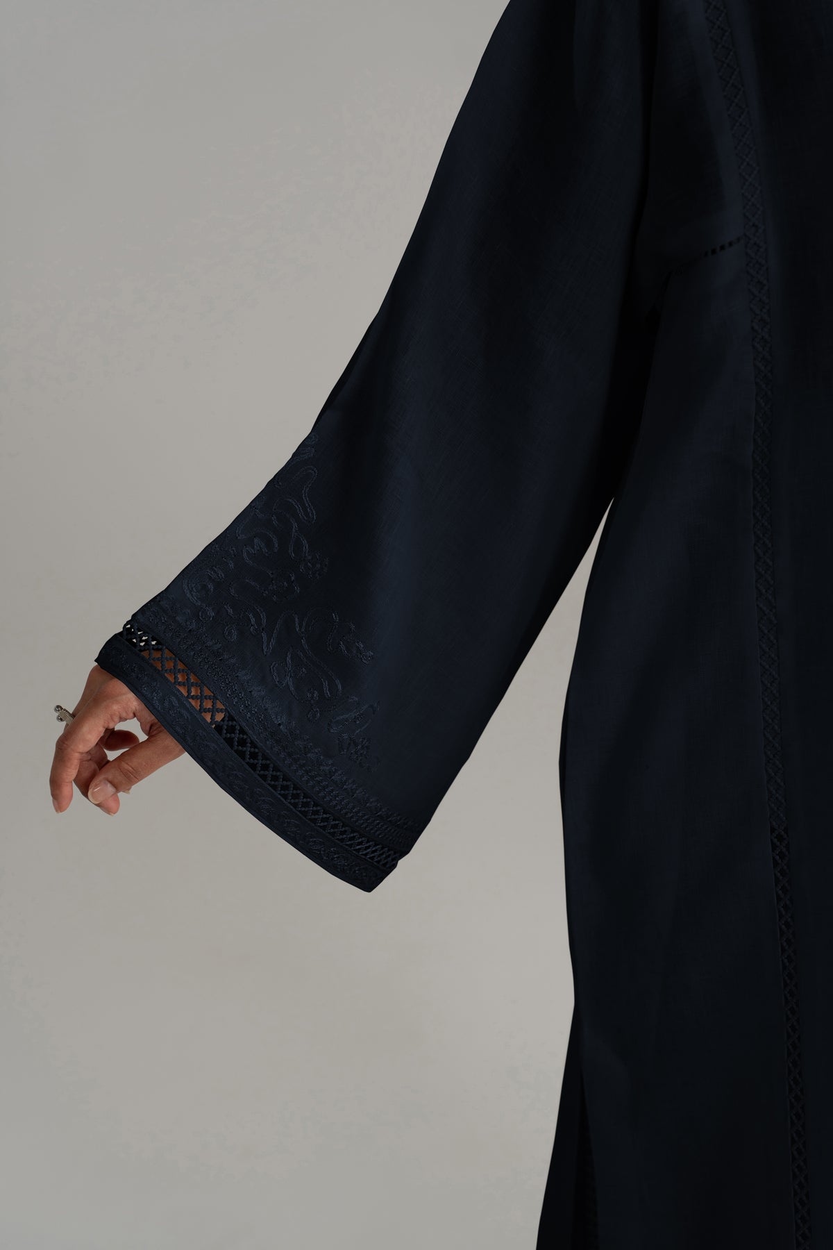 A close-up view of a dark brown long-sleeved garment, showing the embroidered, lace-trimmed cuff of the sleeve.