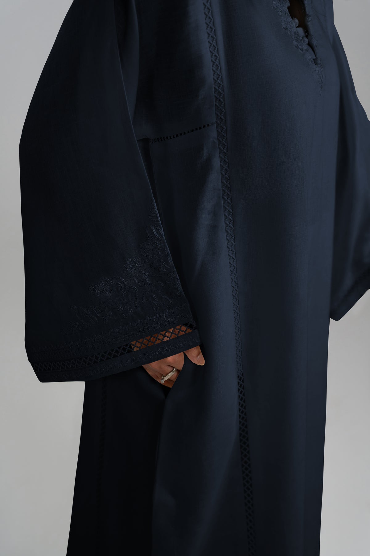 A close-up of a person wearing a dark navy linen set with wide sleeves, featuring delicate lace trim at the cuffs and the pocket.