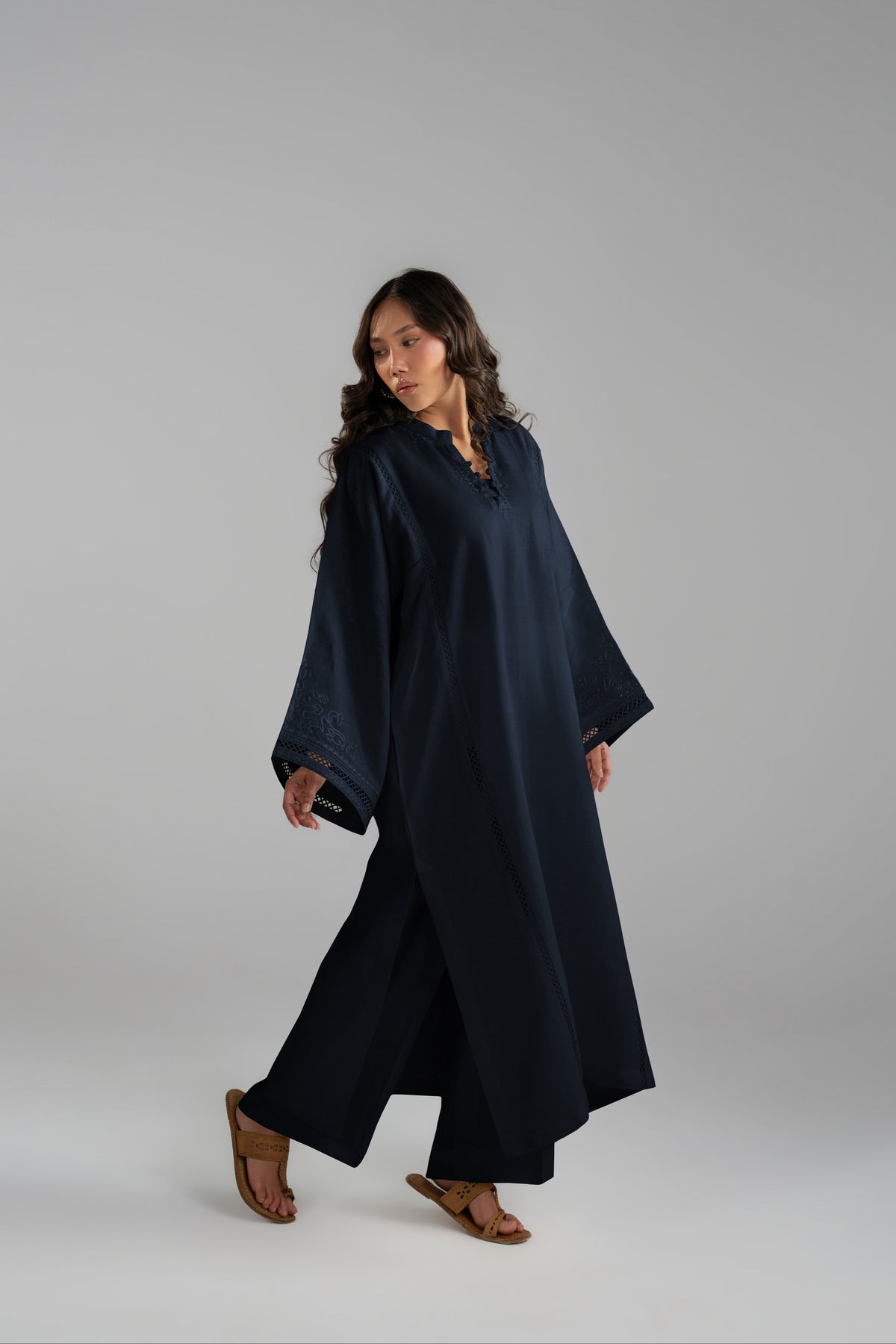 A woman modeling a long, loose-fitting navy blue tunic pure linen dress with wide sleeves and a split neckline, paired with brown leather sandals.