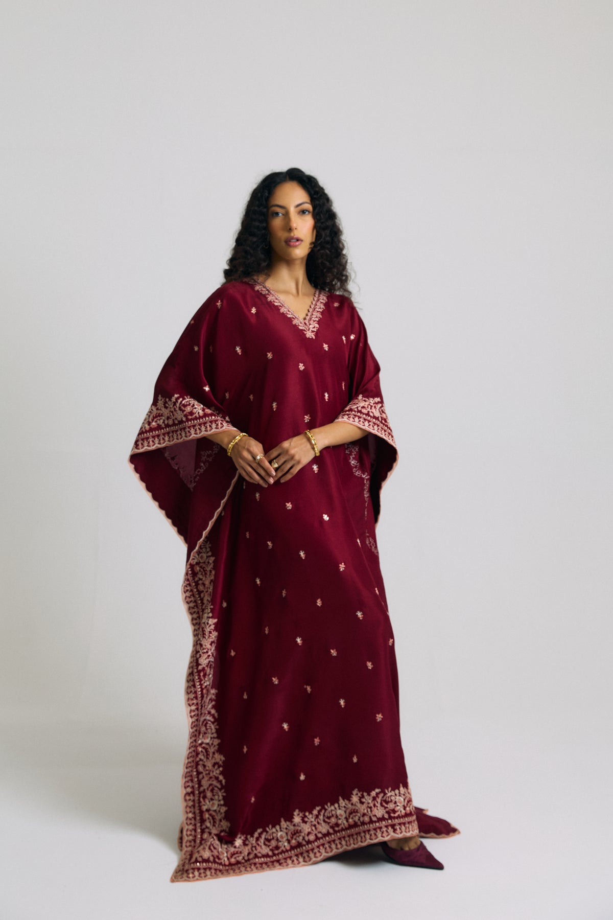 Pakistani kaftan dress in burgundy with wide embroidered sleeves, floral border and hem, three-quarter view