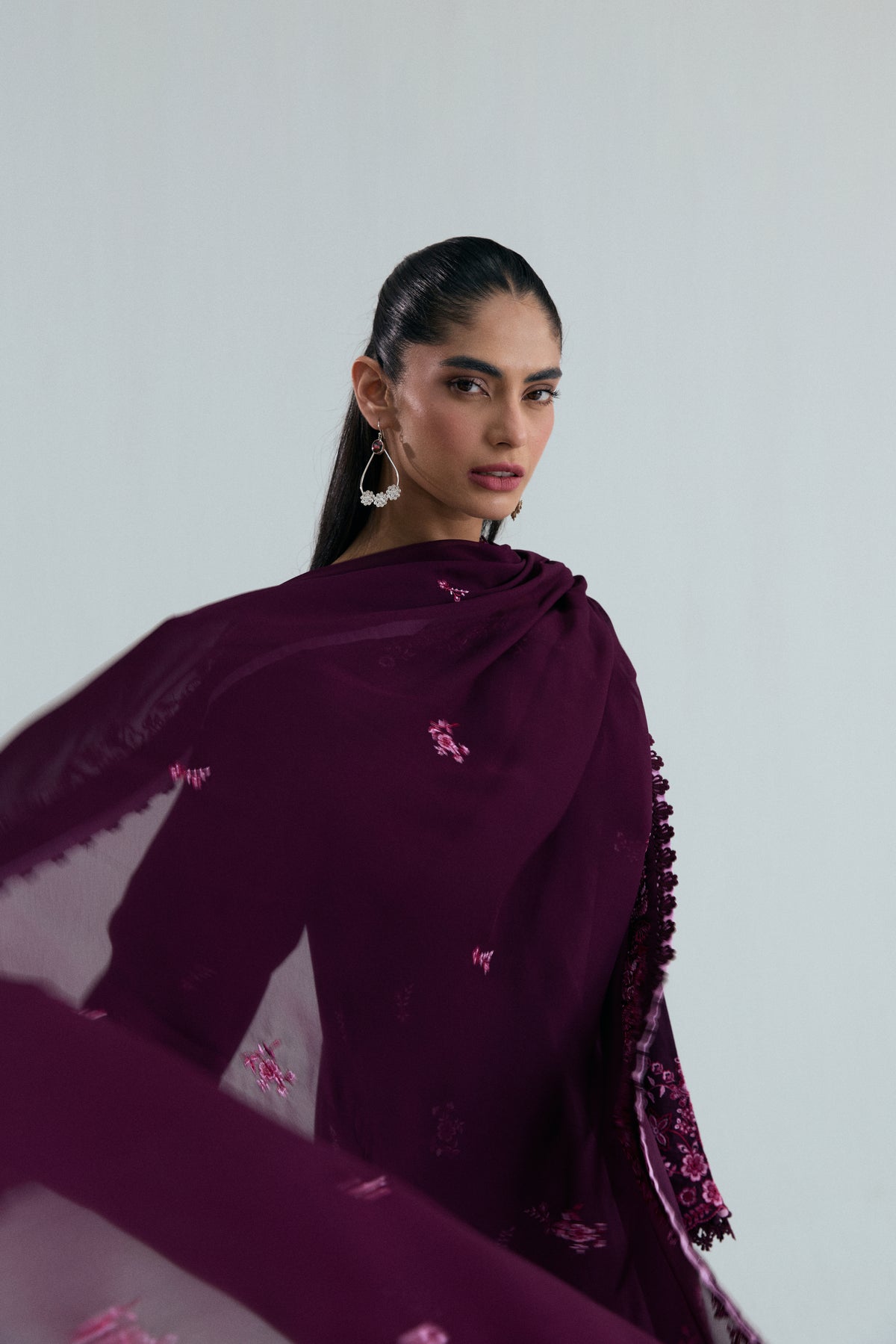 A deep plum-colored kameez, paired with a light, sheer dupatta draped over the shoulder and scattered with floral embroidery.