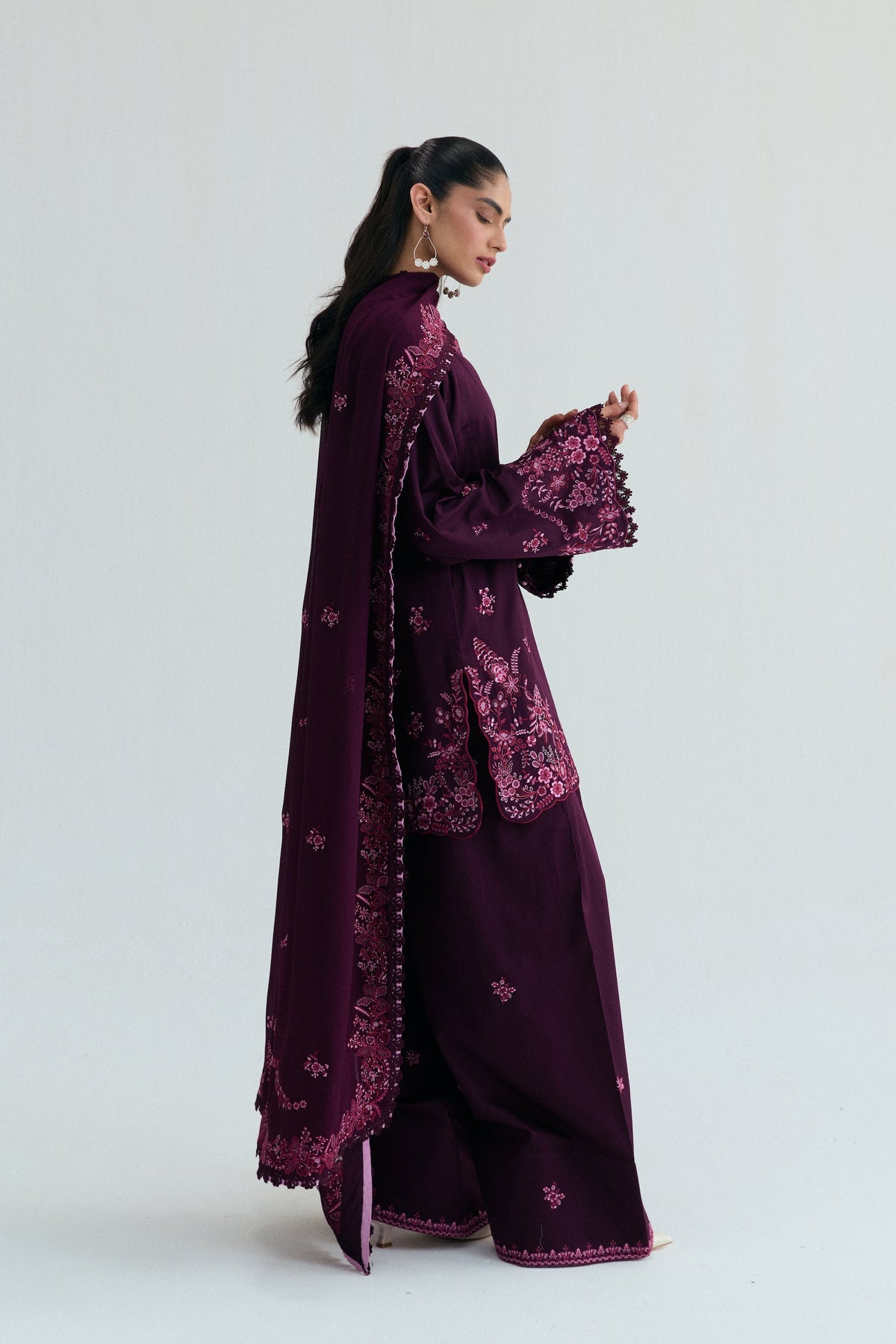 A plum-colored Pakistani suit shown in side profile, featuring embroidered cuffs and a dupatta draped lengthwise.
