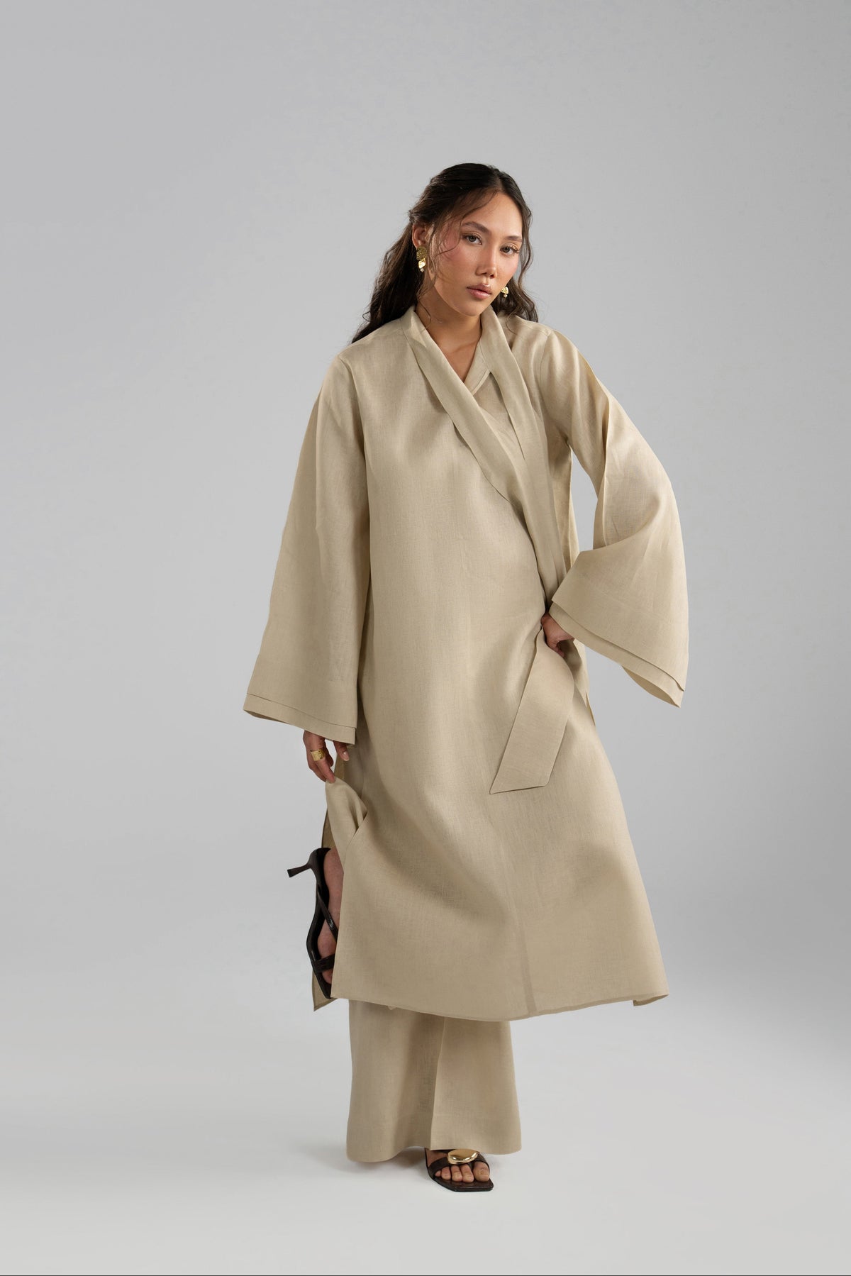 Matching linen trousers and black heeled sandals are visible beneath the side slits of a beige linen tunic.