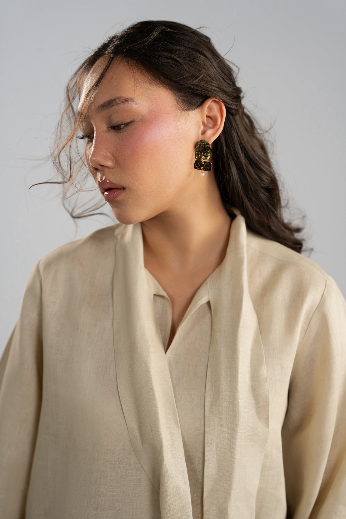 Close-up side view of the stand collar of a linen tunic, styled with prominent gold earrings.