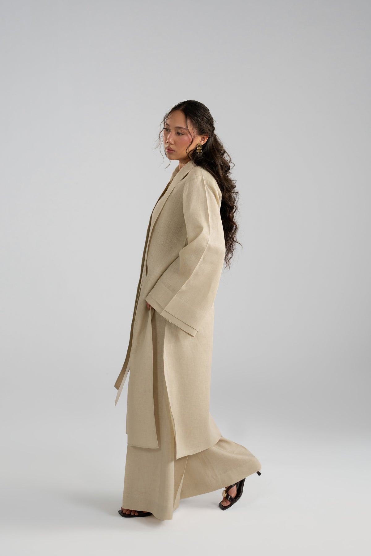 Side profile of the beige linen co-ord in motion, showing the tunic's flowing drape over wide-leg trousers