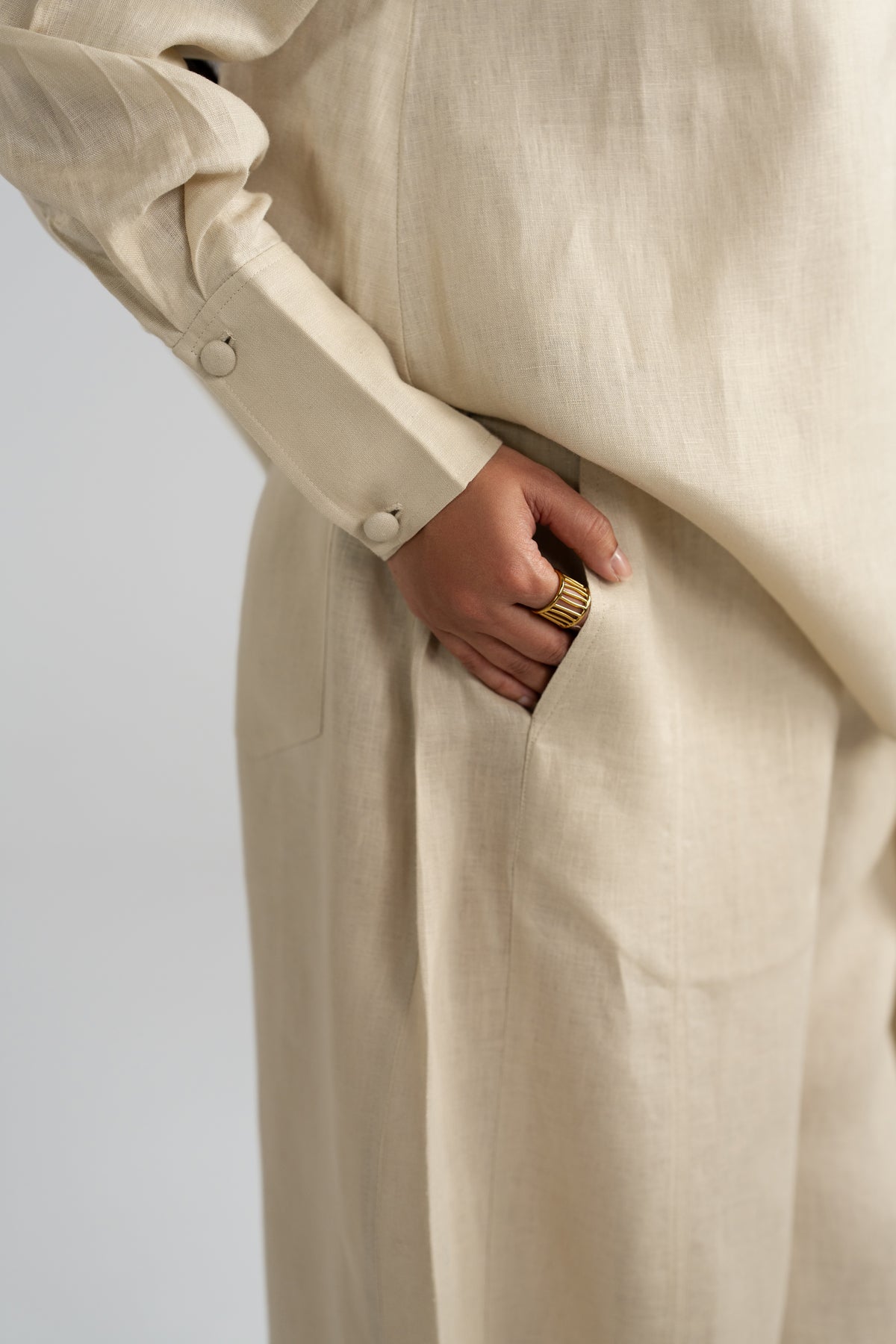 Extreme close-up detail of the Tuscany beige pure linen set, showing the fabric buttons on the sleeve cuff and hand tucked into the trouser pocket.