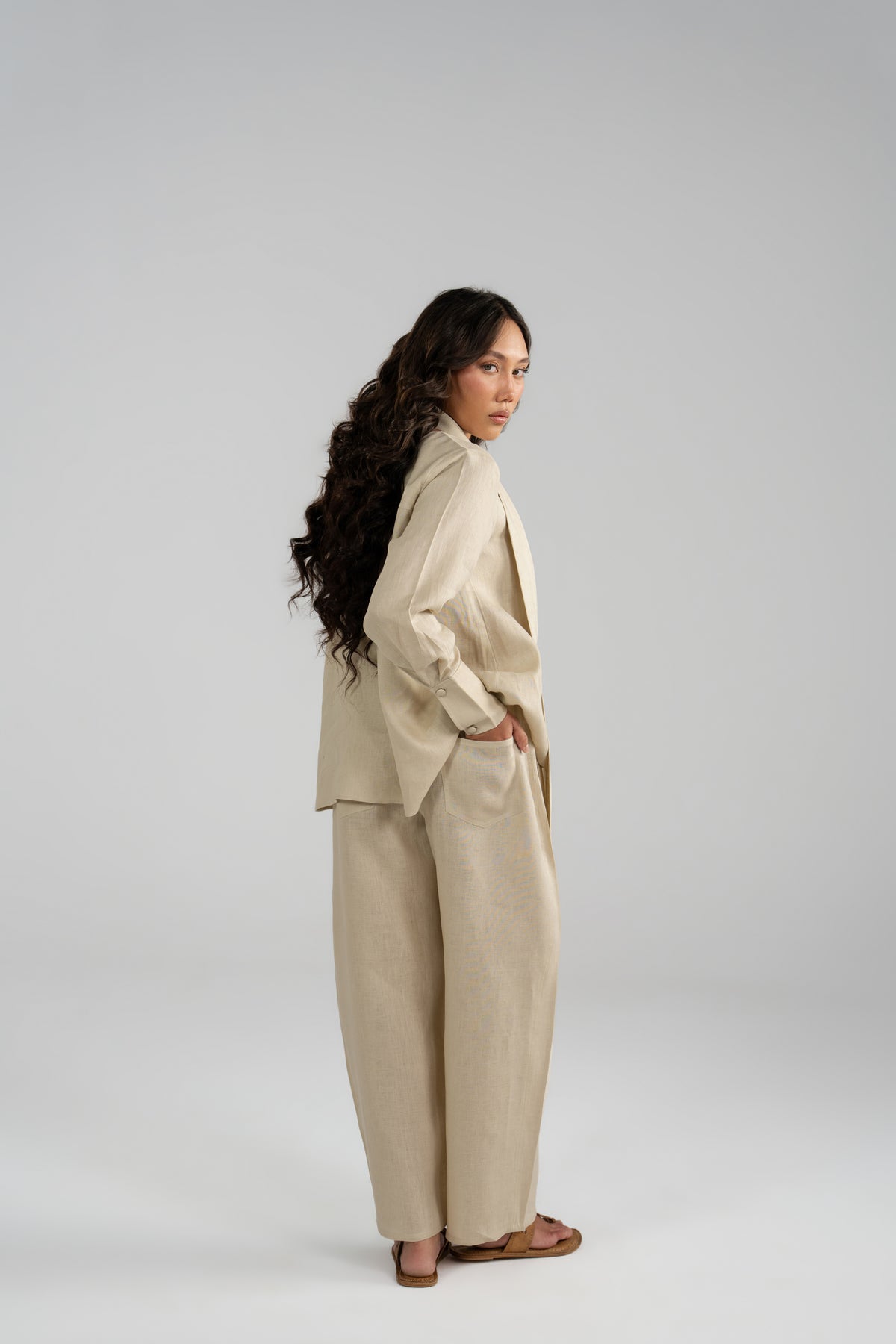 Full-length side view of Tuscany beige pure linen set with a hand in pocket, showcasing the loose shirt drape and wide balloon trousers.
