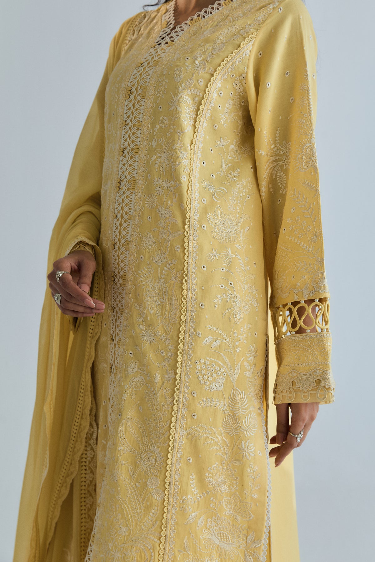 Angled view of ivory embroidery and scalloped lace panel on a yellow Pima cotton kameez